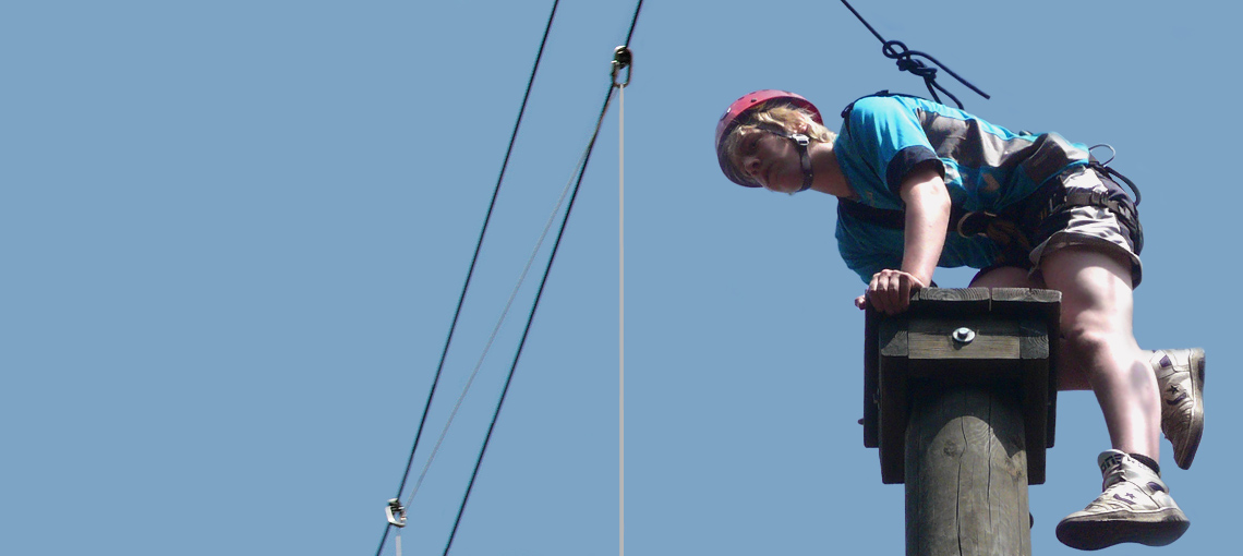 Junge im Kletterpark aufsteigend auf Empore, gesichert am starken Seil